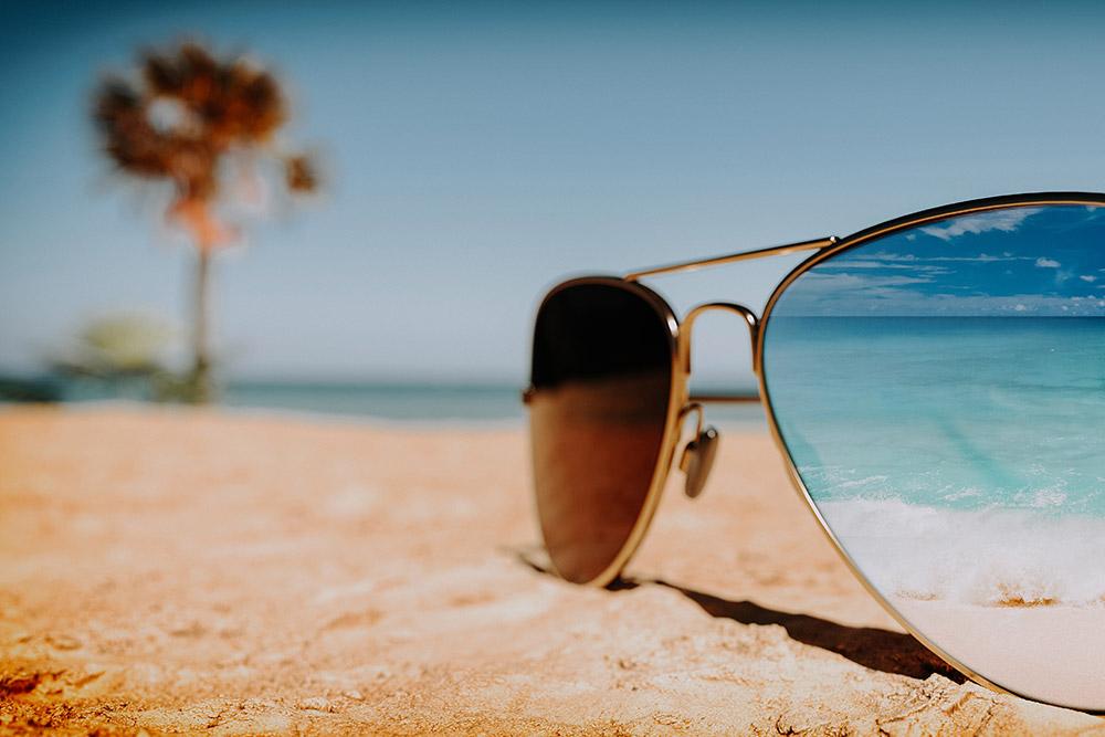 Sunglasses in the sand on the beach with the water and palm tree in the background