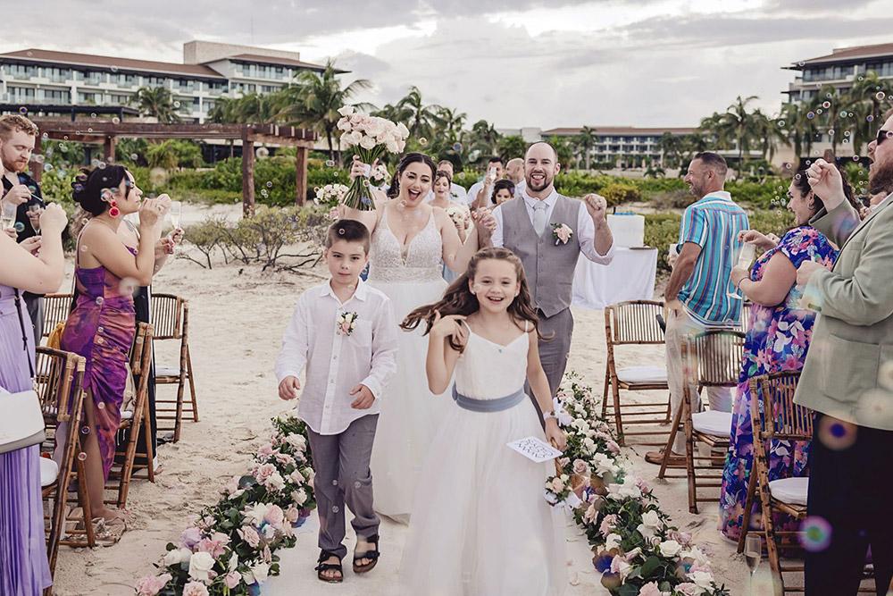 Bride, groom, and wedding party joyfully walk down the wedding isle in front of celebratory guests blowing bubbles at the end of the wedding ceremony.