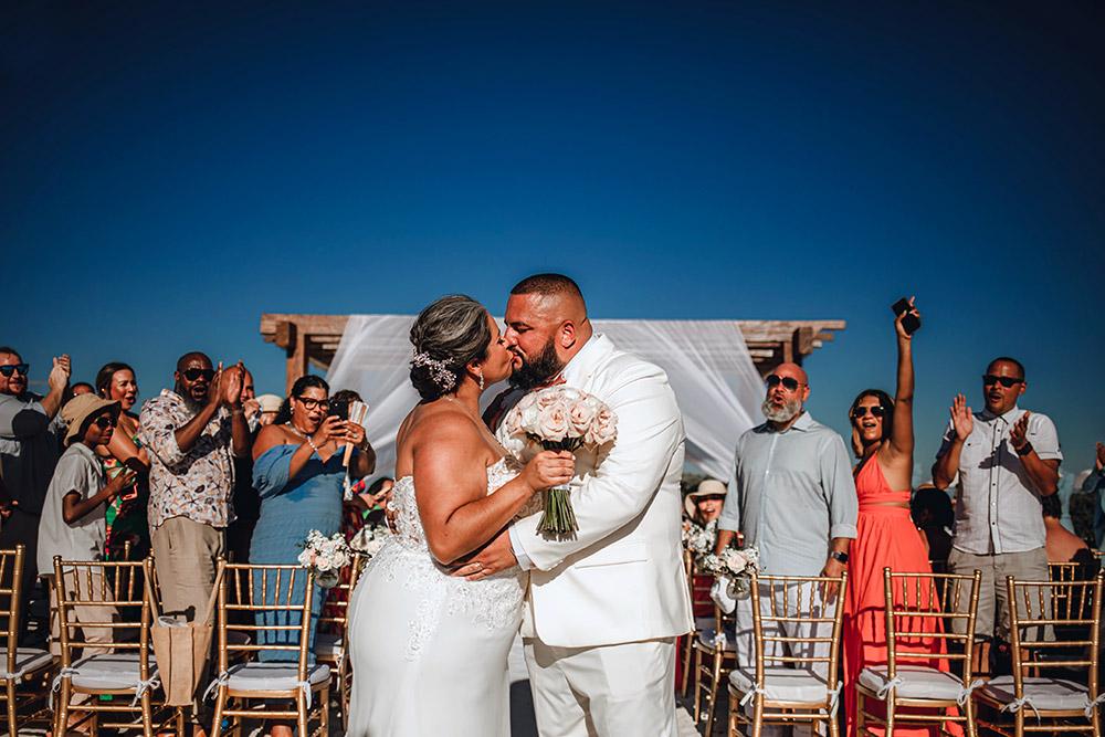 Bride and groom share a kiss at their beachfront wedding in front of joyful guests.