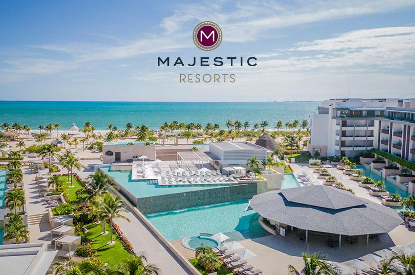 An aerial photograph showcases the Majestic Resorts, a sprawling complex on a white sandy beach next to turquoise ocean waters under a clear blue sky.